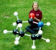 A girl sitting with a giant molecular model on a grass lawn